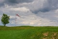 Windsock blown by the wind with overcast sky, lonely tree and green lawn Royalty Free Stock Photo
