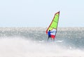Windsurfer on a board with a sail on a water surface shrouded in spray