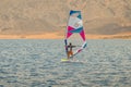 The windsurfer on a board under a sail moves on a calm sea at a low speed,