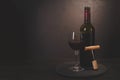 Wine bottle, glass with red wine and cork with corkscrew on dark wooden background. Celebration concept. Copy space. Toned Royalty Free Stock Photo