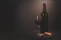 Wine bottle, glass with red wine and cork with corkscrew on dark wooden background. Celebration concept. Copy space. Toned Royalty Free Stock Photo