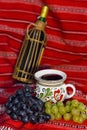 Wine bottle, traditional mug filled with red wine and red and white grapes on a traditional Romanian carpet Royalty Free Stock Photo