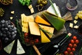 Wine, cheese and snacks on a black stone background. Assorted cheese. Top view.