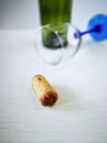 Wine cork is lying on a white wooden table. In the background, an overturned glass with a blue leg and an empty wine bottle. Royalty Free Stock Photo