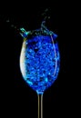 A wine glass with blue cocktail and ice cubes on a black background