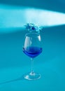 Wine glass with blue liquid and spring flower above it. Strange lights and shadows making scene. Blue performance aesthetic Royalty Free Stock Photo