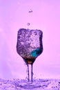 Wine glass with bubbling and splashing water on a pink-purple background. Selective focus