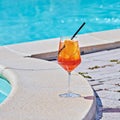 Wine Glass of cold cocktail Aperol spritz against turquoise water of poolside