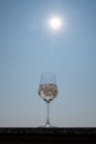 A wine glass with ice cubes stands on a balcony railing with sky and sun Royalty Free Stock Photo