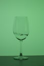 Wine glass on a long stem. A little drink is poured into it, a splash is visible. In back green