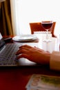 Wine glass with red wine and laptop computer with hands on the keyboard, depth of field, background blur Royalty Free Stock Photo