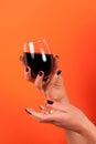 Wine glass in women hand with black nail isolated on orange background Royalty Free Stock Photo