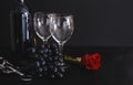 2 wine glasses, a bottle of red wine, a bunch of dark grapes, a metal corkscrew, a red rose on a black background Royalty Free Stock Photo