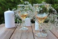 Wine glasses decorated with flowers, and candles on a wooden table on a blurred green natural background in the summer garden. Royalty Free Stock Photo