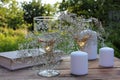 Wine glasses decorated with flowers, old book, and candles on a wooden table on a blurred green background in summer garden Royalty Free Stock Photo