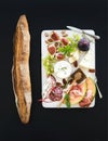 Wine and snack set. Baguette, figs, grapes, nuts, cheese variety, meat appetizers, herbs on white wooden board over
