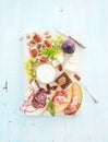 Wine snack set. Figs, grapes, nuts, cheese variety, meat appetizers and herbs on light blue background, top view.