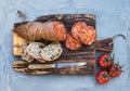 Wine snack set. Hungarian mangalica pork salami sausage, rustic bread and fresh tomatoes on dark wooden board over a