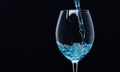 Wineglass filling with water with splashes on black background. Refreshing drink concept. Glass with blue water pouring Royalty Free Stock Photo