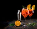 Wineglass of ice cold Aperol spritz cocktail served in a wine glass, decorated with slices of orange and rosemary branch. Black