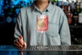 Wineglass with pink drink decorated by pieces of rose petals and green plant standing on bar counter.