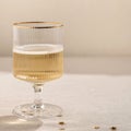 Wineglass with sparkling wine on neutral beige linen background with natural sunlight shadows and gold confetti. Holiday