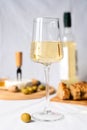 A wineglass of white wine and an olive on the table. In the background in blur a bottle of wine, camembert cheese, baguette and Royalty Free Stock Photo