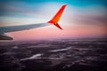 The wing of an airplane flying above the clouds over dark brown ground at dawn. White-orange plane flies at dusk against the Royalty Free Stock Photo