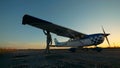 Wing of an airplane is getting inspected by a male aviator on a sunset background