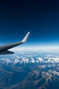 Wing of plane flying over clouds and mountains. Royalty Free Stock Photo