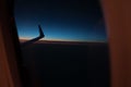 Wing of plane from window porthole at the twilight sky.