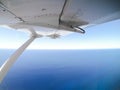 A wing on a small aircraft in flight, Passenger`s perspective looking at blue Ocean endless horizontal through a plane window.