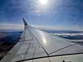 Wing view scene from the left wingside of aeroplane flying in sunny day with blue sky and sun lens flare Royalty Free Stock Photo