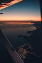 Wing view of a small plane flying at sunset over the city and the sea shore Royalty Free Stock Photo