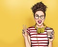 Winking woman in glasses with head phones makes peace gesture Pop art girl holding coffee cup.