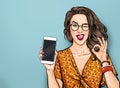Winking woman in glasses showing smart pone and OK sign. Pop art girl holding phone. Digital advertisement female model