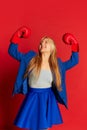 Winner emotions. Young business woman or happy student wearing blue suit and red boxing gloves over bright red Royalty Free Stock Photo