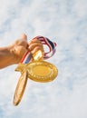 winner hand raised and holding two gold medals against blue sky.