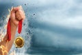 Winner raising hand with gold medal from fire flames up to stormy sky, closeup. Space for text