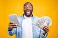 Winner! Young rich african american man in casual t-shirt holding money dollar bills with surprise isolated over yellow wall