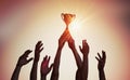 Winning team is holding trophy in hands. Silhouettes of many hands in sunset Royalty Free Stock Photo