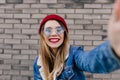 Winsome caucasian girl in denim jacket making selfie with smile. Lovable white lady in red hat taki Royalty Free Stock Photo