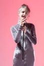 Winsome Expressive Singing Caucasian Girl In Gray Reflective Dress Posing With Microphone On Pink Background