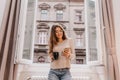 Winsome girl in casual attire spending time at home and posing on city background with cup of tea. Graceful lady in Royalty Free Stock Photo