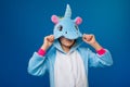 Winsome girl playfully posing in unicorn costume. Studio shot of emotional woman in kigurumi having fun on blue background