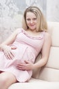 Pregnancy Concepts. Winsome Romantic Caucasian Pregnant Blond Female Resting on Couch With Hands on Belly Indoors