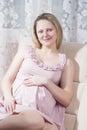 Winsome Romantic Caucasian Pregnant Blond Female Resting on Couch With Hands on Belly Indoors