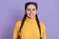 Winsome smiling lady with dark hair and two pigtails looking directly at camera with charming smile, wearing yellow sweater,