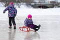 Happy elder girl pulling her young sister on a sled on the ice in snowy winter park Royalty Free Stock Photo