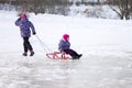 Happy ittle girl pulling her young sister on a sled on the ice in snowy winter park Royalty Free Stock Photo